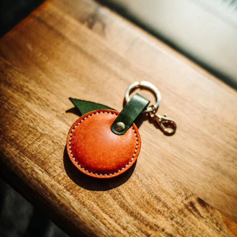 PU leather orange keychain with metal ring stitching and leaf pendant detail PU leather orange keychain with metal ring stitching and leaf pendant detail